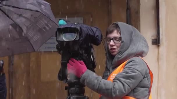 СЕНТ-ПЕТЕРБУРГ, РОССИЯ - 15 ДЕКАБРЯ 2018 года: На улице стоят две женщины в оранжевых жилетах с зонтиком и видеокамерой — стоковое видео