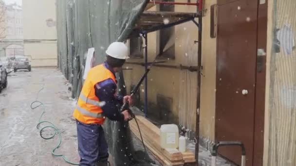 Sankt Petersburg, Ryssland-december 15, 2018: konstruktion man Worker bär uniform och hjälm sprutar vatten till husets fasad — Stockvideo