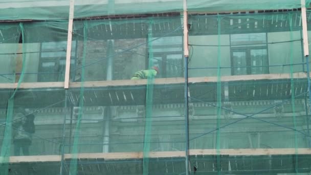 Sankt Petersburg, Ryssland-december 15, 2018: byggnadsarbetare i enhetligt arbete på byggnadsställningar täckta med grönt nät — Stockvideo