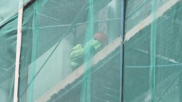 Saint petersburg, russland - dez 15, 2018: bauarbeiter in uniform arbeitet auf einem gerüst, das mit grünem netz bedeckt ist — Stockvideo