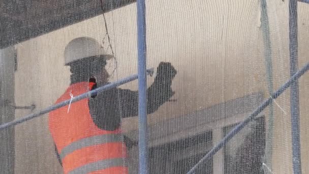 Saint petersburg, russland - dez 15, 2018: mann arbeiter in orangefarbener uniformweste zerkratzt wand mit hammer auf gerüst — Stockvideo
