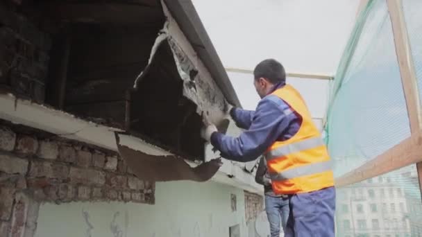 SAINT PETERSBURG, RUSSIE - 10 AVRIL 2018 : Un travailleur asiatique en uniforme orange brise un vieux mur en bois sale . — Video