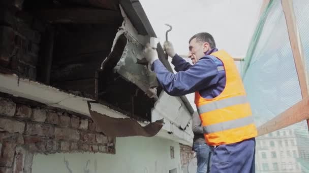 サンクトペテルブルク、ロシア - 4月 10, 2018: オレンジ色のベストを着たアジアの建設男性労働者は汚れた古い木製の壁を壊します. — ストック動画