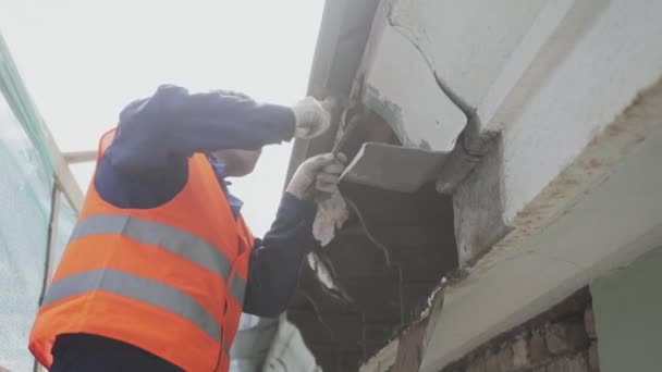 SAN PETERSBURG, RUSIA - 10 DE ABRIL DE 2018: Trabajador varón maduro en uniforme naranja y casco desprende sucia pared de madera vieja . — Vídeos de Stock