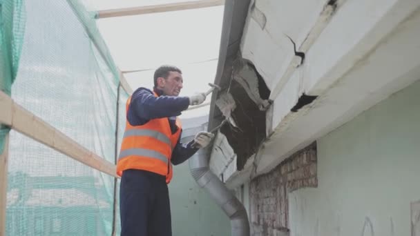 サンクトペテルブルク、ロシア - 4月 10, 2018: オレンジ色のユニフォームとヘルメットのアジアの男性労働者は汚れた古い木製の壁を壊します. — ストック動画