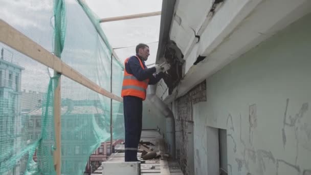 SAN PETERSBURG, RUSIA - 10 DE ABRIL DE 2018: Obrero asiático vestido de naranja y casco rompe pared de madera vieja y sucia . — Vídeo de stock