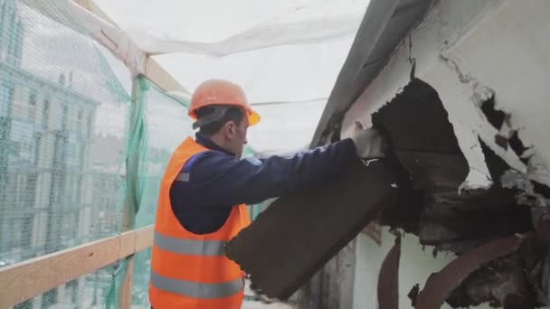 St. petersburg, russland - 10. april 2018: bauarbeiter in orangefarbenem schutzanzug durchbricht schmutzige alte hölzerne wand. — Stockvideo