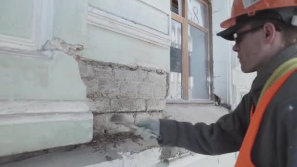 Санкт-Петербург, Росія-10 квітня 2018: чоловічий працівник в помаранчевих рівномірних фарбах шматок цегляної стіни з великим пензлем. — стокове відео