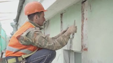 Saint Petersburg, Rusya - 10 Nisan 2018: Turuncu yelek ve kask giyen erkek işçi duvara metalik ağ monte etti.