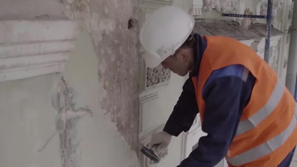 САЙНТ-ПЕТЕРБУРГ, РОССИЯ - 10 апреля 2018 года: Рабочий в оранжевом жилете и в белых шлемах с молотком часть белой стены — стоковое видео