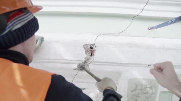 SAN PETERSBURG, RUSIA - 10 DE ABRIL DE 2018: Trabajador en traje naranja trabaja con un pequeño martillo para golpear una pieza de la pared de la fachada — Vídeos de Stock