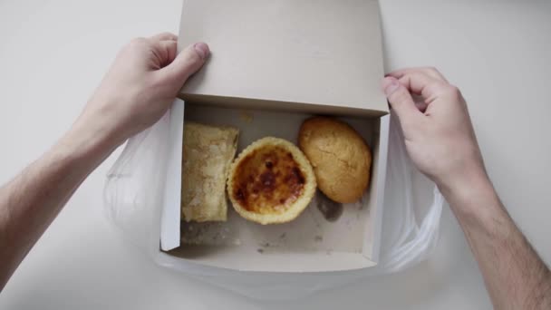 Les mains des hommes tiennent sac en plastique blanc avec boîte en papier blanc avec gâteau et petits pains . — Video