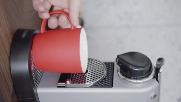 Alguém mão coloca copo vermelho na bandeja de pequena máquina de café automática com vagens . — Vídeo de Stock