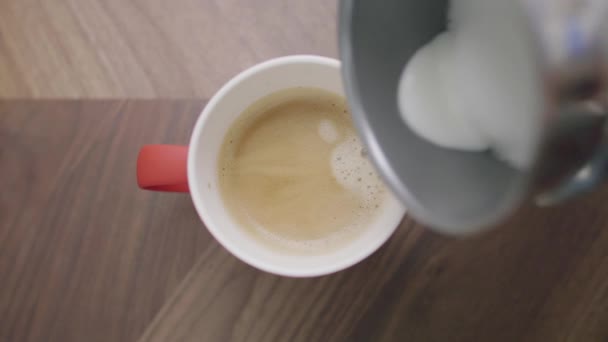 Someones hand lägger mjölk till röd kopp med kaffe placeras på träbord — Stockvideo