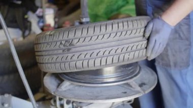 Yetenekli adam oto tamircisi otomobil servis garajında araç tekerleğine lastik koyar.