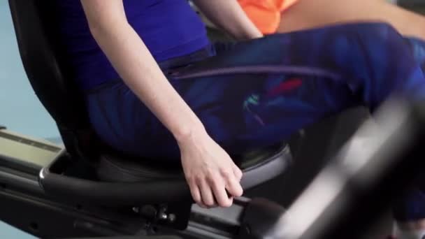 Piernas de deportistas haciendo ejercicio cardiovascular en el ciclo estacionario en el gimnasio . — Vídeos de Stock