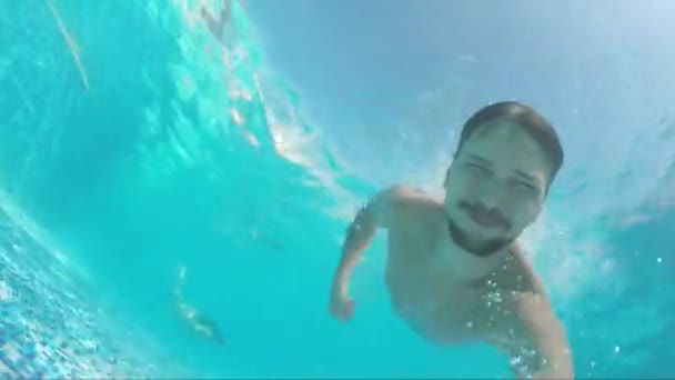 Giovane barbuto bell'uomo sta nuotando sotto l'acqua blu in piscina — Video Stock