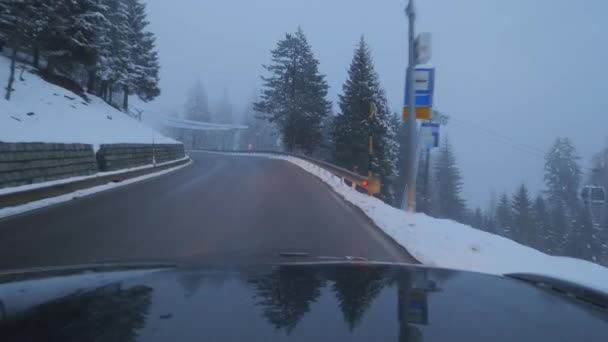 눈 덮인 나무와 언덕 사이 교외 지역에서 도로에 검은 자동차이동. — 비디오