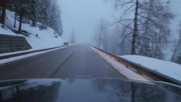 Μαύρο αυτοκίνητο κινείται στο δρόμο σε προάστιο ανάμεσα σε χιόνι καλυμμένα δέντρα και λόφους. — Αρχείο Βίντεο