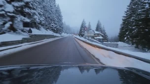 Carro escuro se move na estrada em área de subúrbio entre árvores cobertas de neve e colinas . — Vídeo de Stock