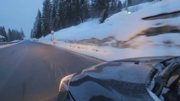 Чорний автомобіль з фарами на ходах по дорозі вздовж снігових покритих дерев і пагорбів . — стокове відео