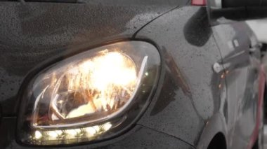 Yağmurlu bir günde yanıp sönen farlar ile boş sokakta siyah modern araba çekim.