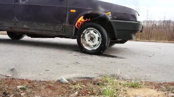 Oude Violet auto is achtergelaten op de verlaten grijze weg met brandende wiel op koude dag. — Stockvideo
