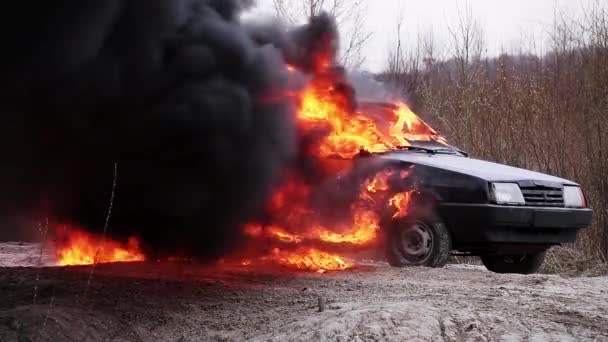 Ogromny palenie płomień ognia w pełni pali brudny stary samochód w lewo na opuszczonej drodze. — Wideo stockowe