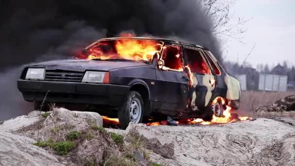 Masivní oranžový ohnivý plamen úplně spálí staré špinavé auto na šedé silnici — Stock video