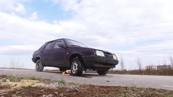 Velho carro violeta enferrujado é deixado na estrada deserta com roda em chamas no dia frio . — Vídeo de Stock