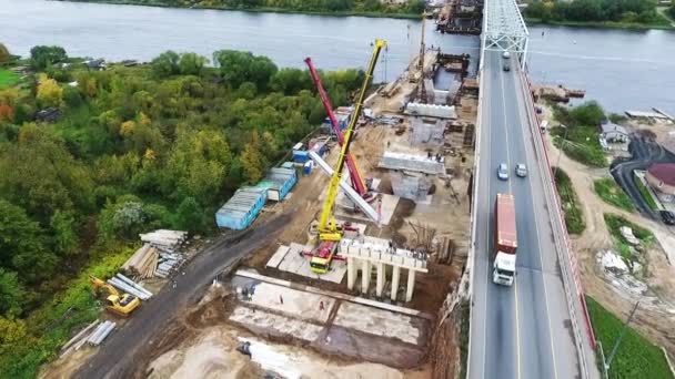 Petrohrad, Rusko-20. září 2018: letecký pohled na stavbu mostu v oblasti se dvěma jeřáby poblíž silnice a řeky — Stock video