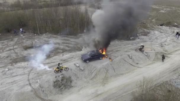 Sky View van brandende auto in verlaten stof velden met bewegende motorrijders rond. — Stockvideo