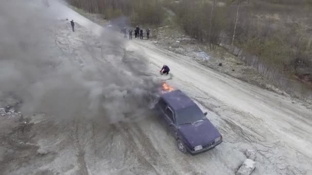 Égő autó elhagyatott pormezők a mozgó motorbicikkerek és figyeli az emberek — Stock videók