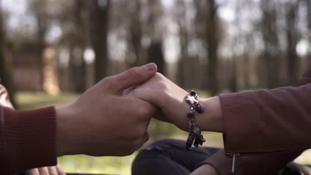 Mão caras está romanticamente segurando as meninas mão vestindo pulseira agradável, no parque . — Vídeo de Stock