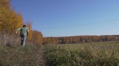 Yeşil giysili genç adam kırsal bölgede tek başına koşuyor.