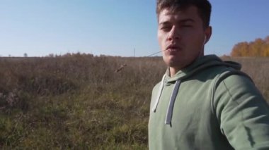 Ağızda sapı olan yakışıklı beyaz adam tarla boyunca kırsalda yürüyor.