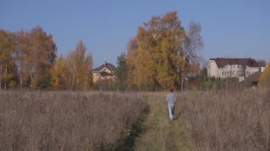 Kamera, erkeğin sarı kuru tarlaların arasında kırsal alandaki evlere doğru yürüdüğünü gösteriyor..