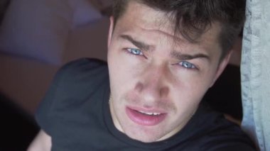 Siyah tişörtlü, mavi gözlü, kameraya dik dik bakan beyaz bir adamın yüzü..