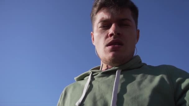 Beau jeune homme blanc gesticule à la caméra sur fond de ciel bleu . — Video