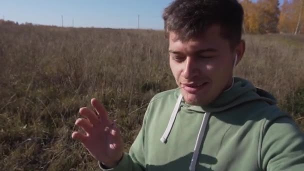Милий молодий чоловік зі стеблом в роті йде в сільській місцевості вздовж поля . — стокове відео