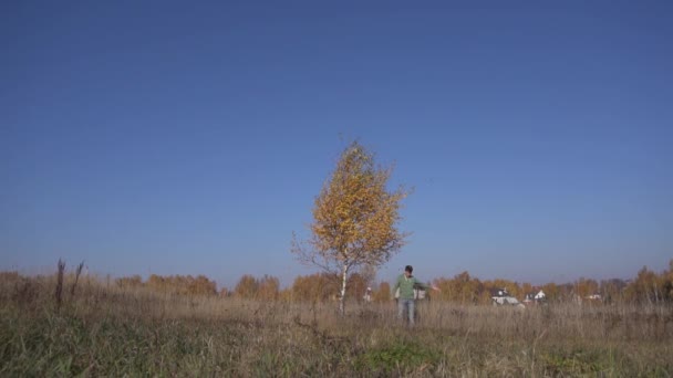 Ansicht des weißen jungen Mannes, der unter einem Baum mit gelben Blättern auf dem Land steht. — Stockvideo
