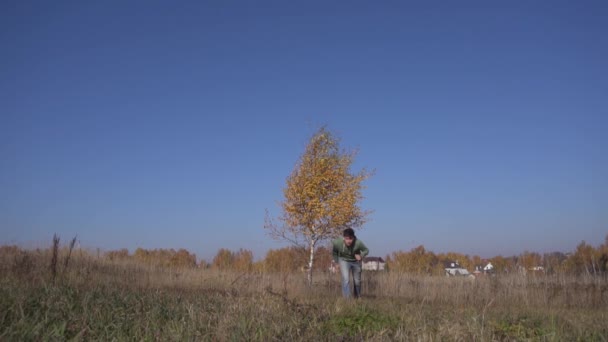 Joven hombre caucásico huye del árbol con hojas amarillas hacia la cámara . — Vídeos de Stock