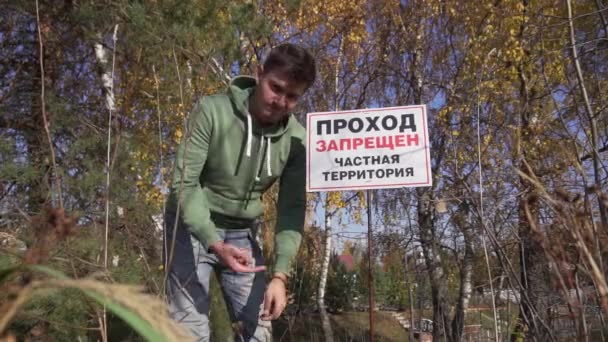 Mladý muž v kapucích ukazuje na velkou ceduli Zakázaná oblast, Soukromý majetek. — Stock video