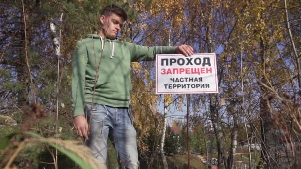 Young cute man in hoodey rotates big sign RESTRICTED AREA, PRIVATE PROPERTY. — Stock Video