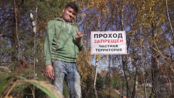 Guy in hoodey shows middle finger next to sign Περιορισμένη περιοχή, Ιδιωτική ιδιοκτησία — Αρχείο Βίντεο