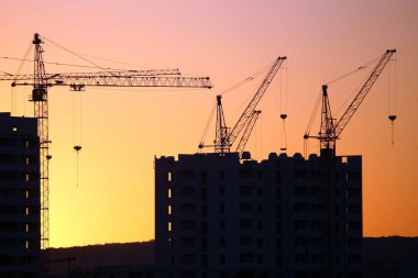 Günbatımı gökyüzünün arka planında inşa edilmiş evler olan vinçler.