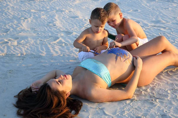 young children paint on the belly of a pregnant mother