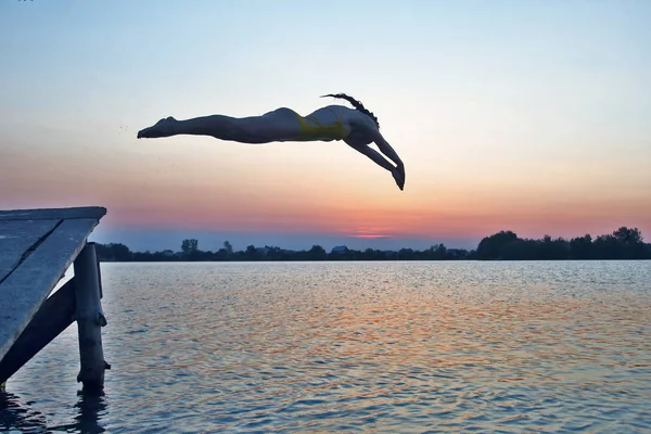 Silhouette of a girl jumping into the water in the evening