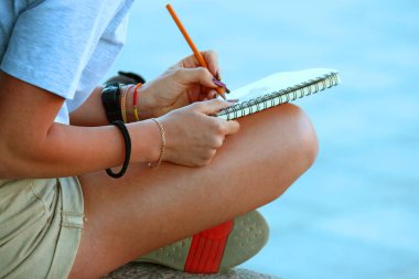 Kız kaldırımda oturan bir defter çizer