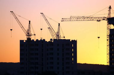 Günbatımı gökyüzünün arka planında inşa edilmiş evler olan vinçler.